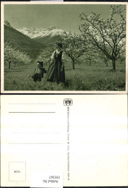 195367, SOS Children's Village 13/56 Woman with boy in traditional dress in a meadow, flowering trees, mountain backdrop