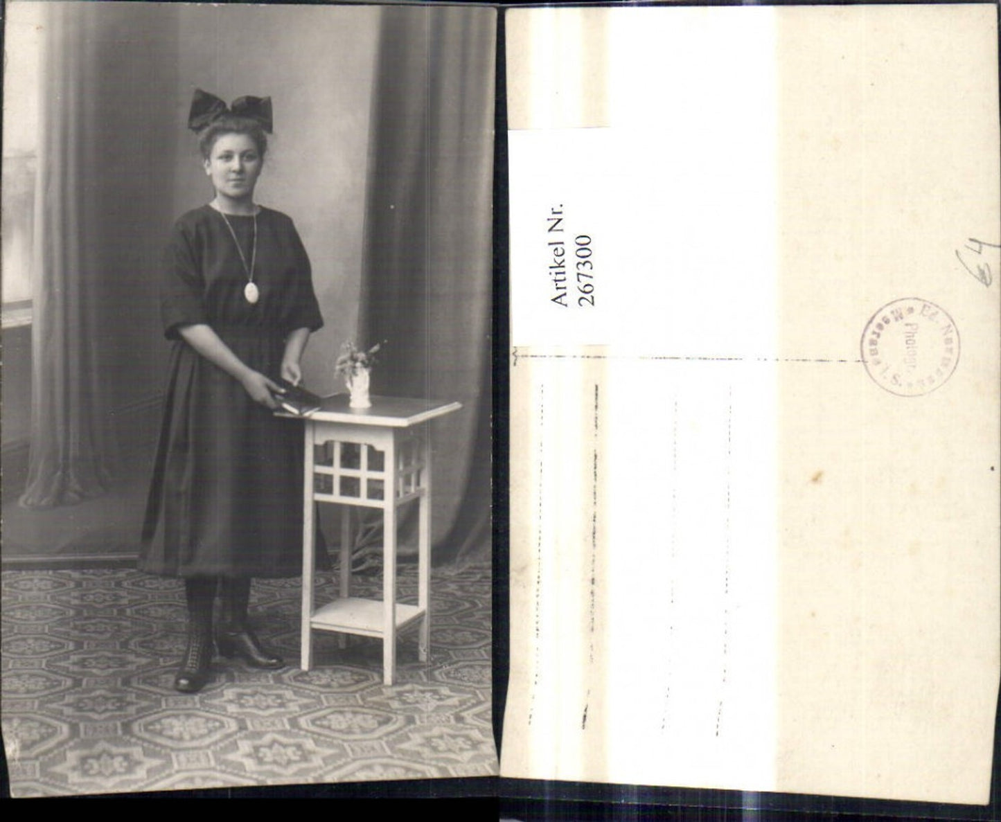 267300,Foto Ak Frau Kleid Haarschleife m. Buch b. Tisch stehend
